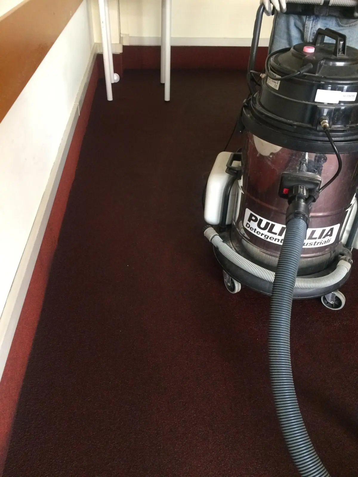 Aspirazione professionale di moquette bordeaux con aspiraliquidi industriale in corridoio