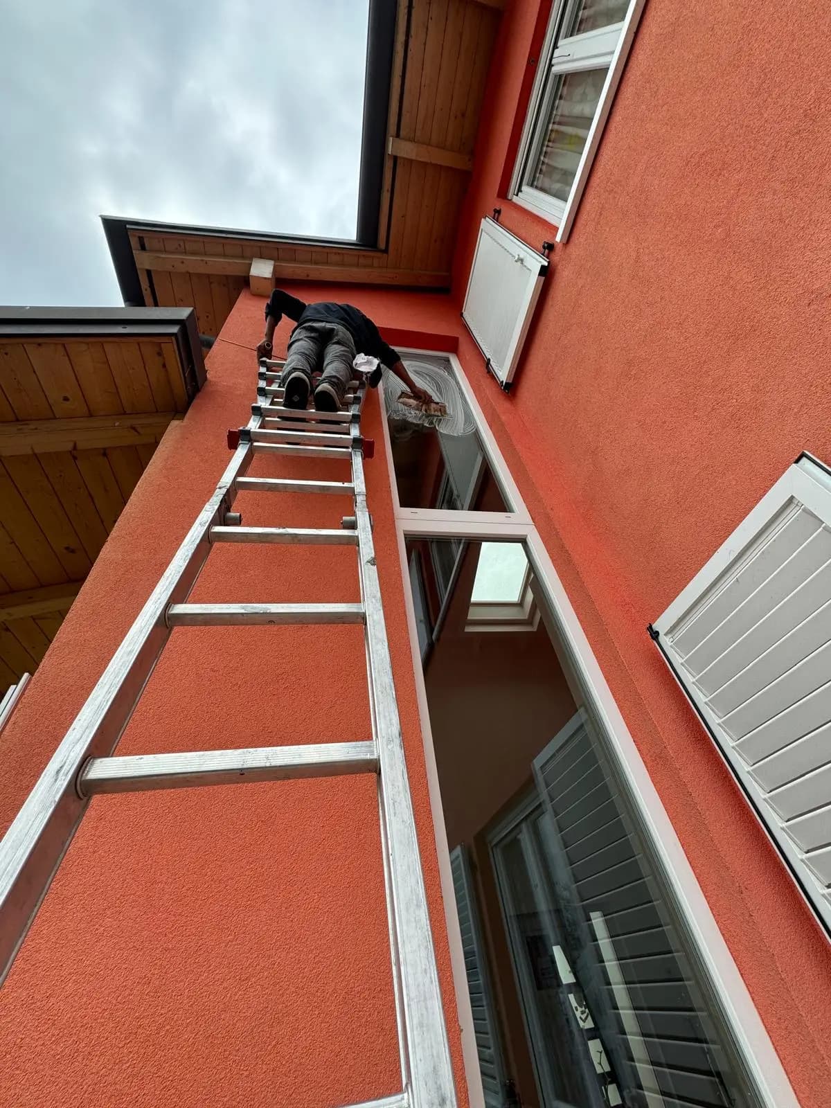Operatore su scala alta per la pulizia di finestre su facciata esterna di edificio residenziale