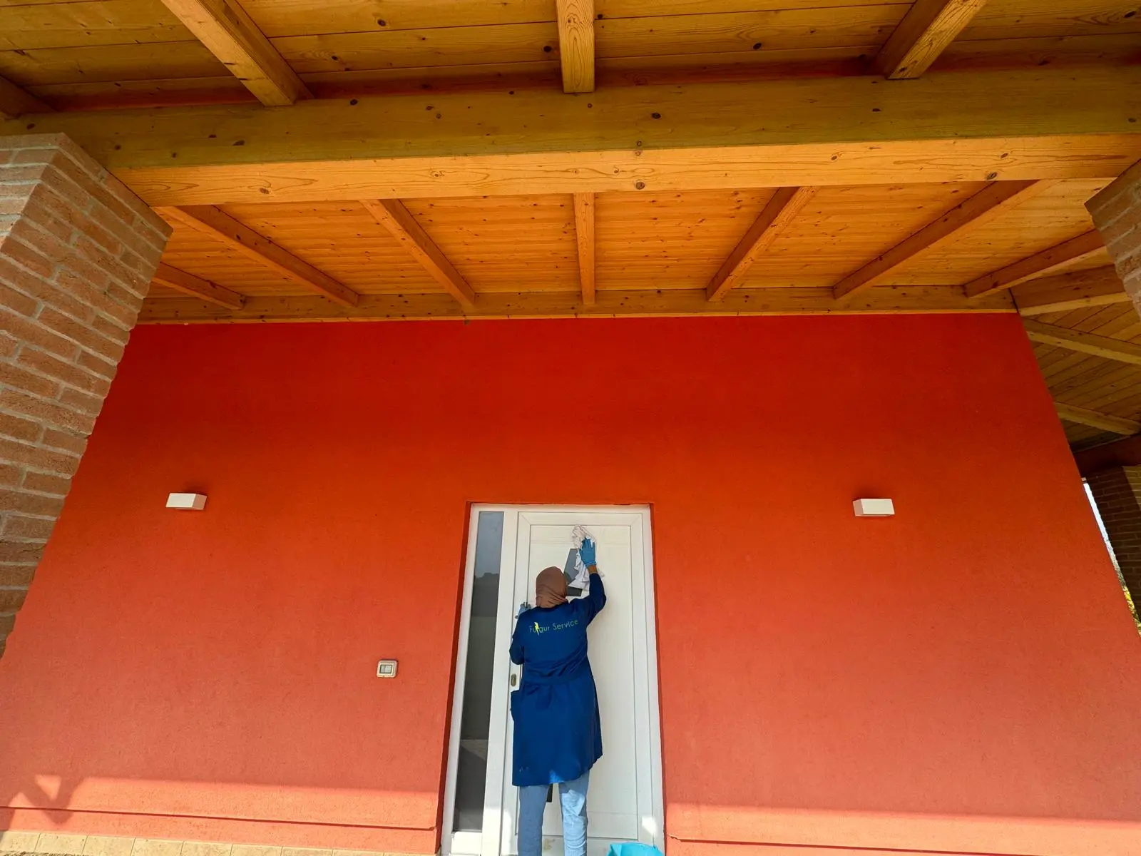 Operatore pulisce serramenti e infissi sulla facciata esterna di una casa con portico in legno