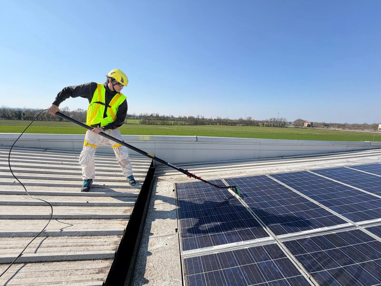 Operatore Fulgur Service con DPI e casco pulisce pannelli fotovoltaici su tetto industriale