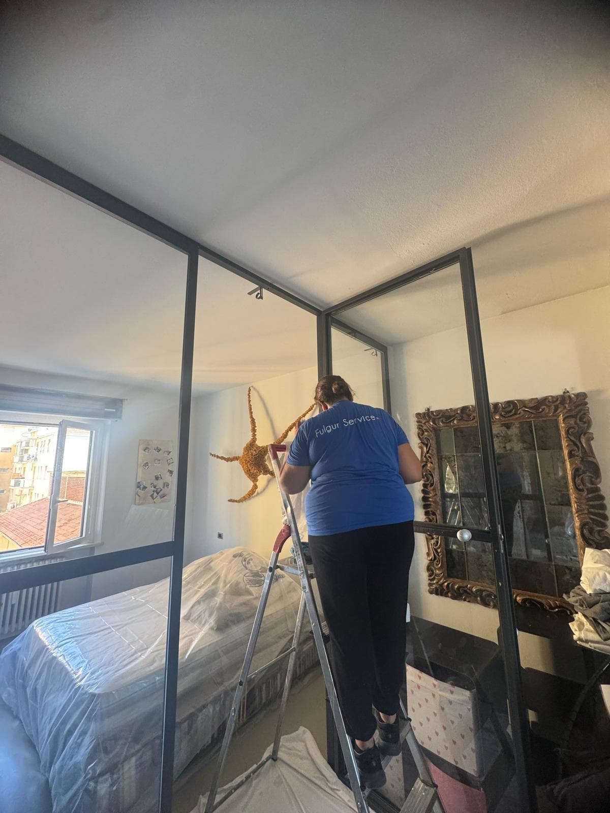 Operatrice Fulgur Service su scala pulisce pareti vetrate in camera da letto di appartamento privato