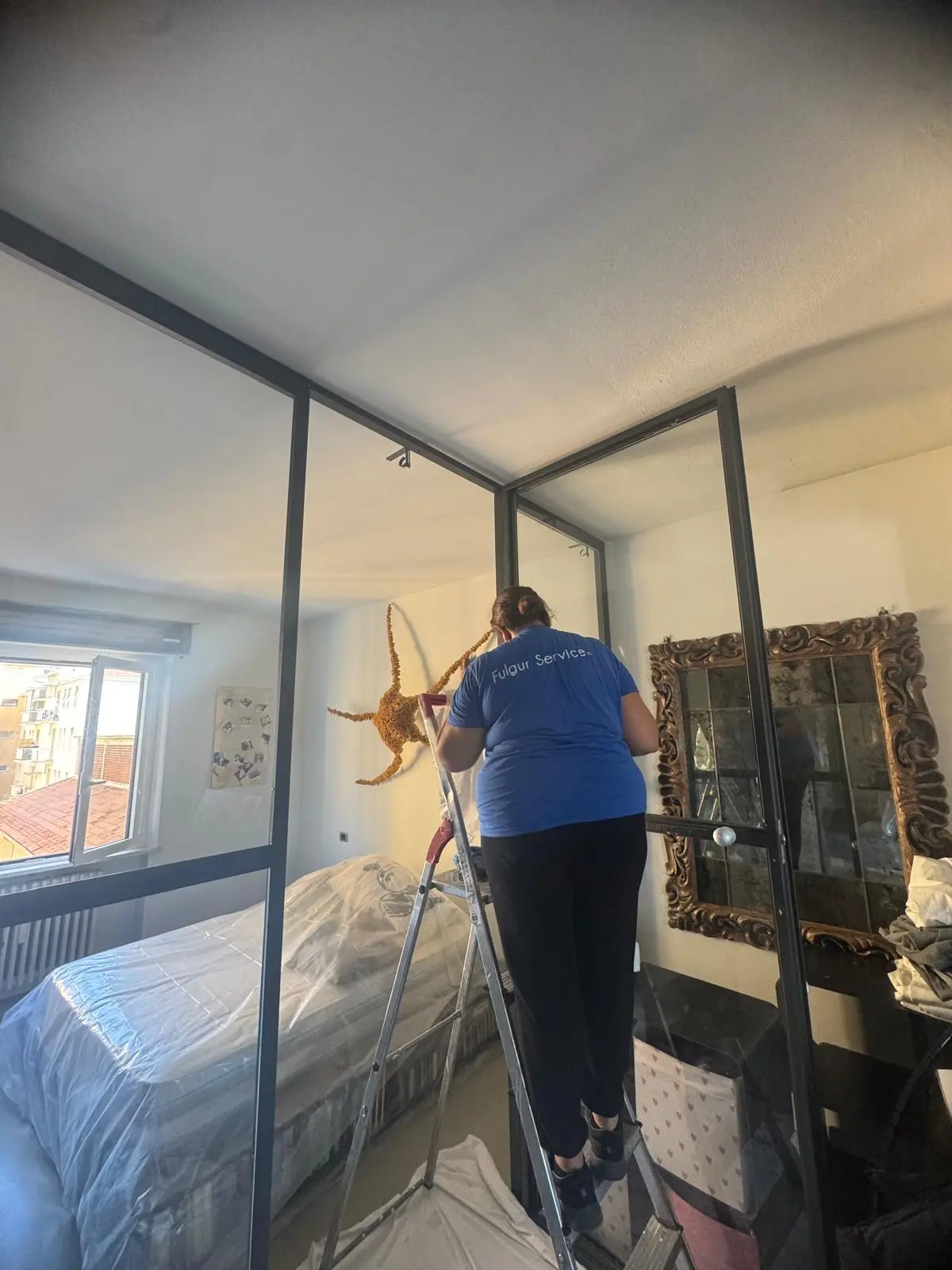 Operatrice Fulgur Service su scala pulisce pareti vetrate in camera da letto di appartamento privato