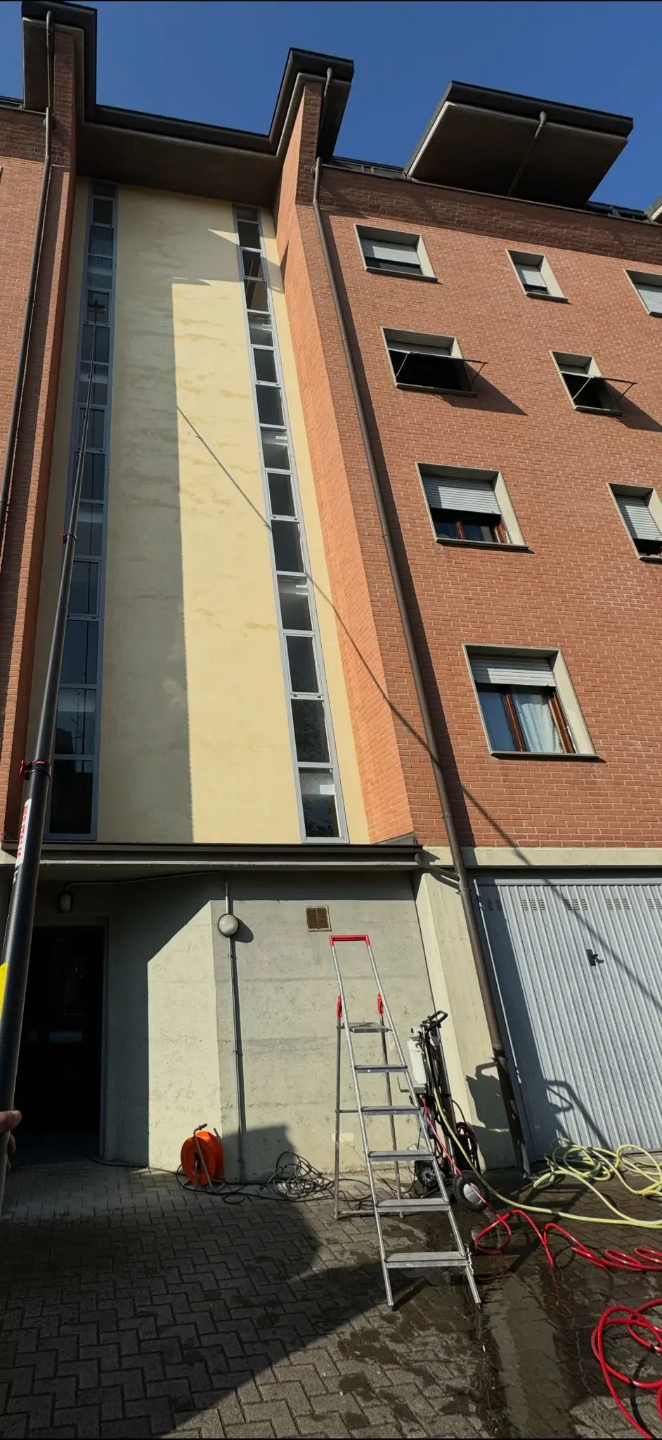 Intervento di pulizia vetrate in quota su facciata di un palazzo moderno con asta telescopica