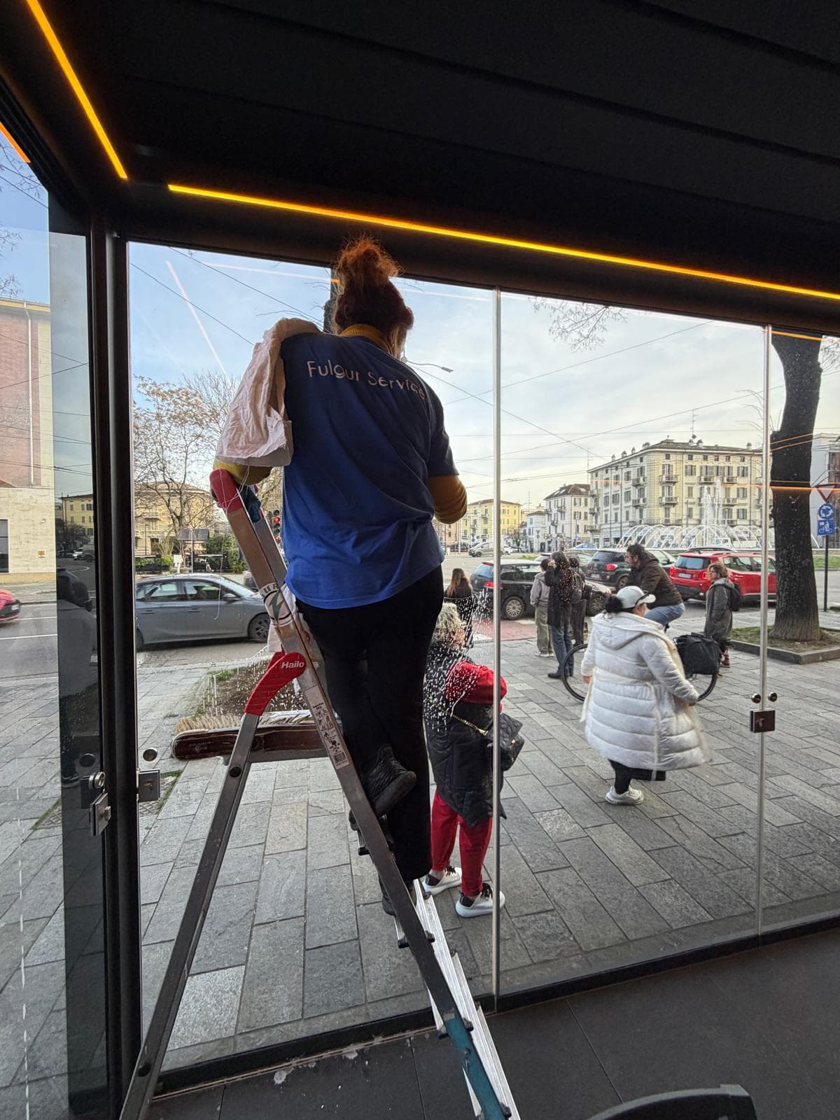 Operatrice Fulgur Service su scala pulisce la vetrina di un negozio nel centro città