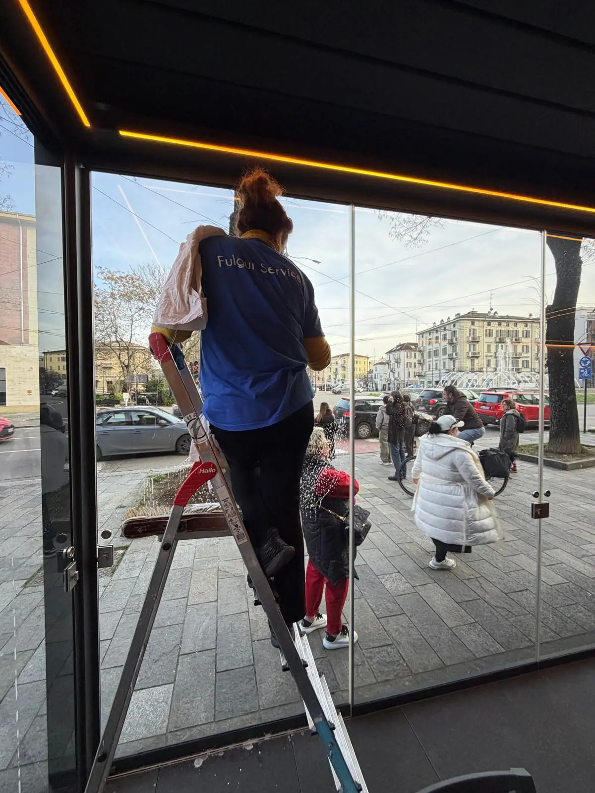 Operatrice Fulgur Service su scala pulisce la vetrina di un negozio nel centro città