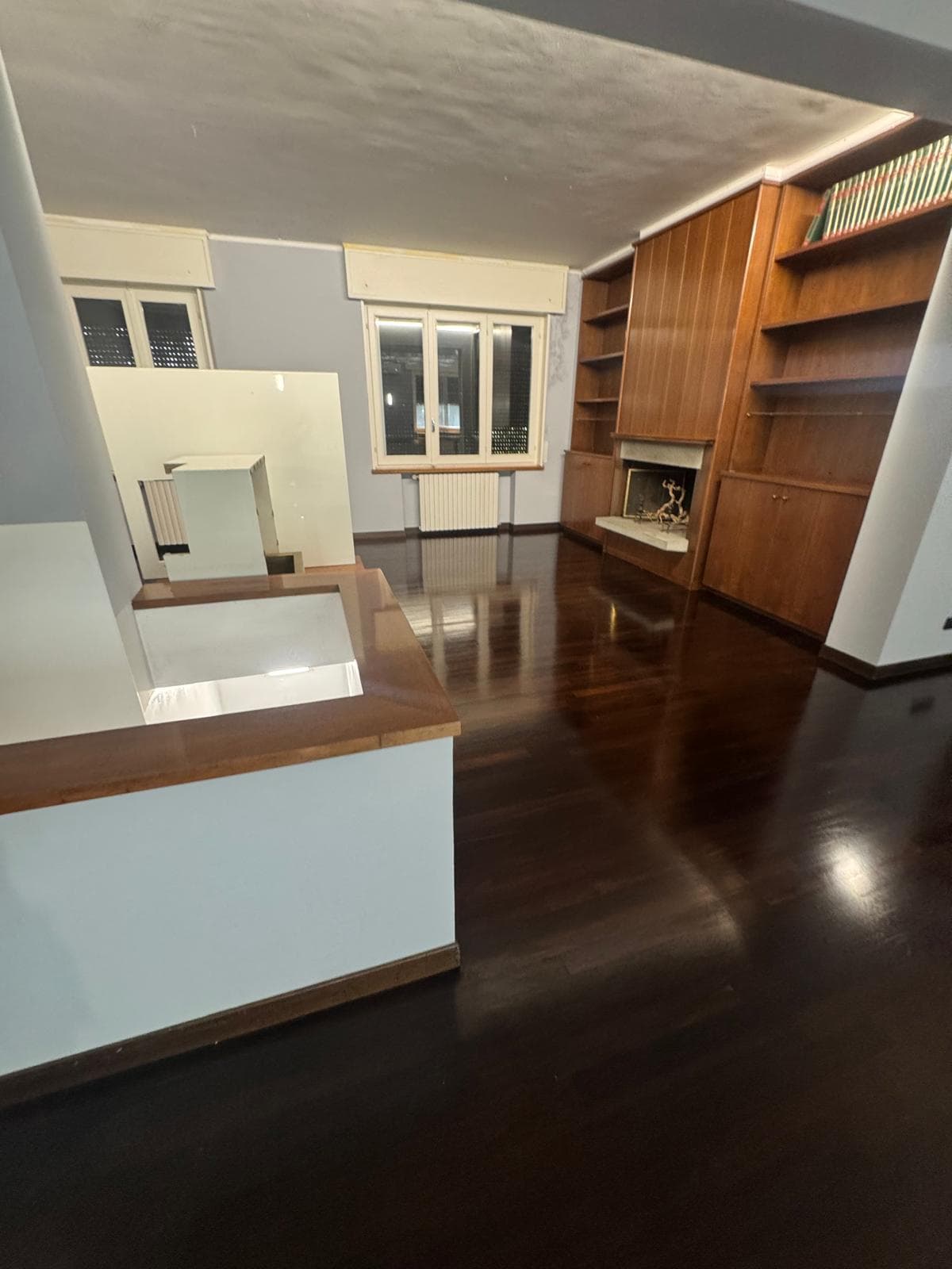 Salone di appartamento con pavimento in parquet scuro lucidato, camino e libreria in legno