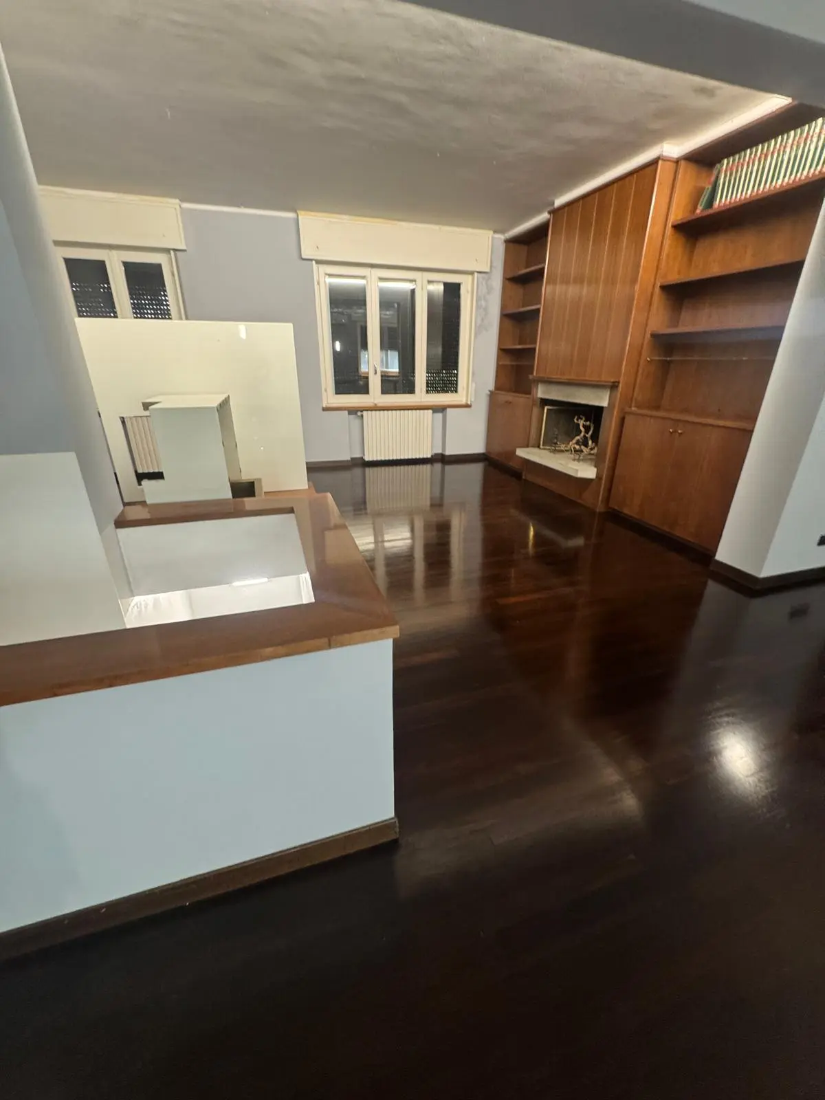 Salone di appartamento con pavimento in parquet scuro lucidato, camino e libreria in legno